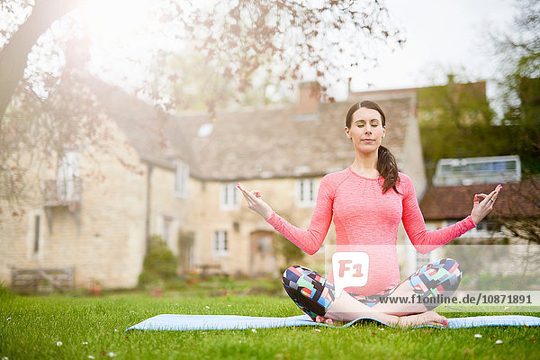 Schwangere Frau sitzt im Freien  in Yogastellung