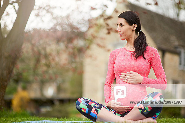 Schwangere Frau sitzt im Freien und hält den Bauch