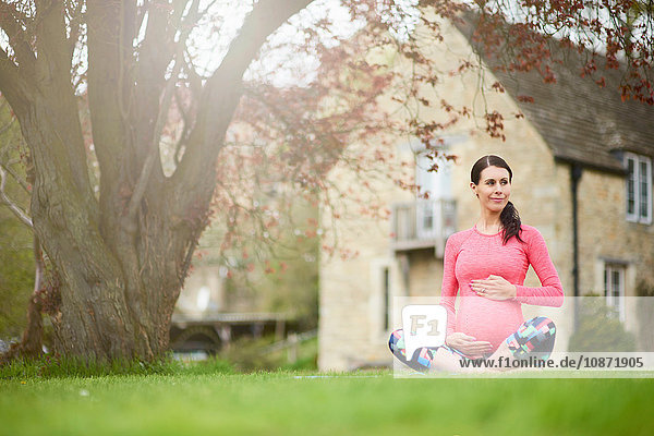 Schwangere Frau sitzt im Freien und hält den Bauch