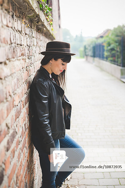 Young woman leaning against brick wall