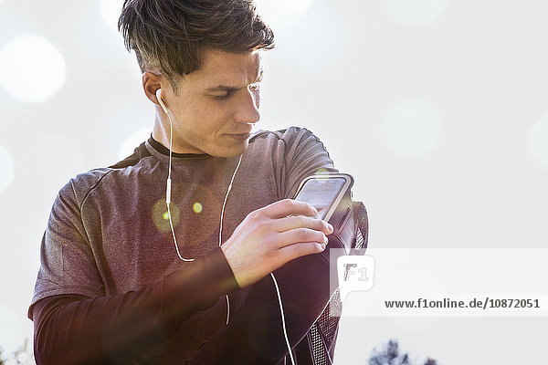 Young man outdoors  adjusting mp3 player on arm