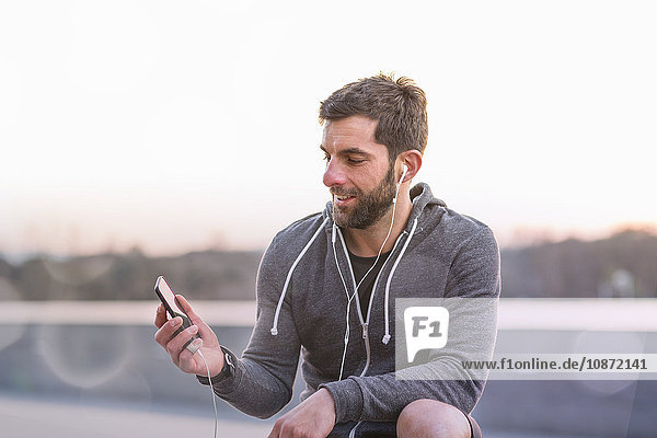 Mittelgroßer erwachsener Mann  im Freien  Smartphone anschauend  Kopfhörer tragend