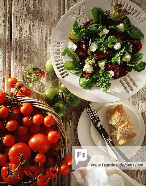 Mittelmeersalat  Fetakäse  schwarze Oliven  sonnengetrocknete Tomaten  Salatblätter mit frischen Tomaten im Korb  Draufsicht