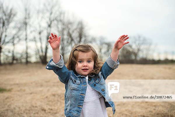 Young girl standing in field  hands in air