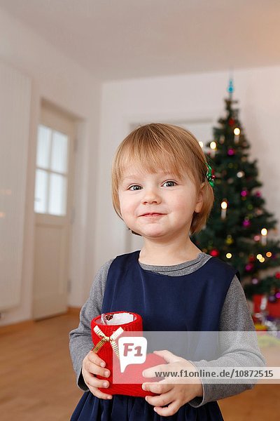 Mädchen vor dem Weihnachtsbaum mit rotem Stiefel in der Hand und lächelndem Blick in die Kamera