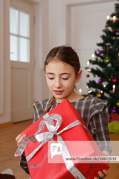 Mädchen vor dem Weihnachtsbaum schaut nach unten und hält Geschenk