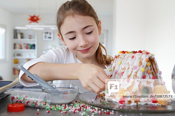 Mädchen an Küchentheke schmückt Lebkuchenhaus lächelnd