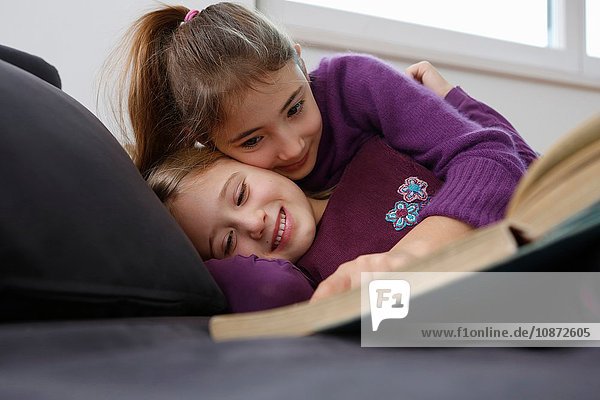 Oberflächenansicht eines Mädchens  das auf dem Sofa liegt und ein Buch liest  sich umarmt und lächelt
