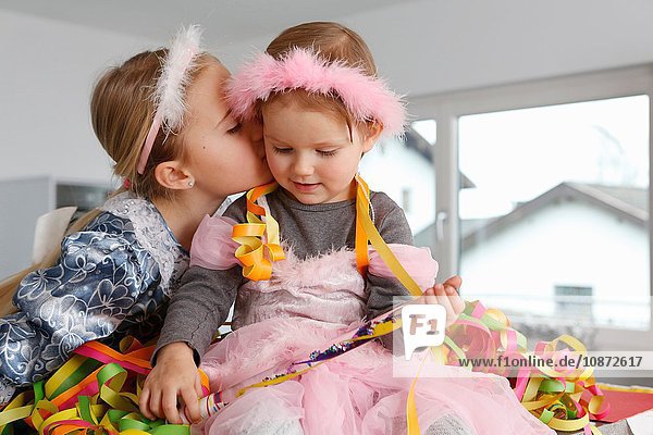 Sisters dressed up as princesses  covered in party streamers  kiss on cheek
