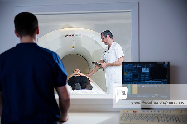 Control room window view of doctor preparing patient on CT-scanner