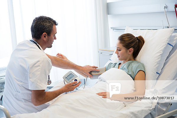 Doctor measuring patients blood pressure on hospital bed