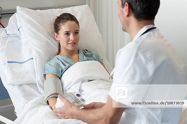 Doctor measuring female patients blood pressure on hospital bed
