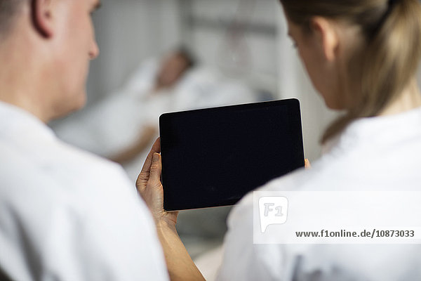 Über-Schulter-Ansicht von Ärzten  die sich ein Fuß-Röntgenbild auf einem digitalen Tablett auf der Krankenhausstation ansehen