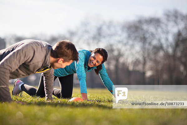 Young man and woman doing push up training on playing field