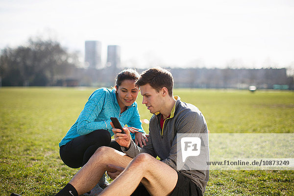 Young man and woman training  reading smartphone texts in park