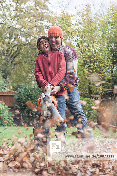 Vater und Sohn beim Laubblasen  um das Herbstlaub zu entfernen  lachen