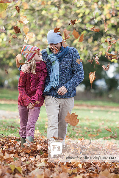 Father and daughter fooling around in park  walking through autumn leaves