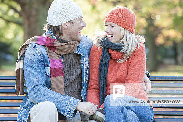Heterosexual couple sitting together on park bench  laughing