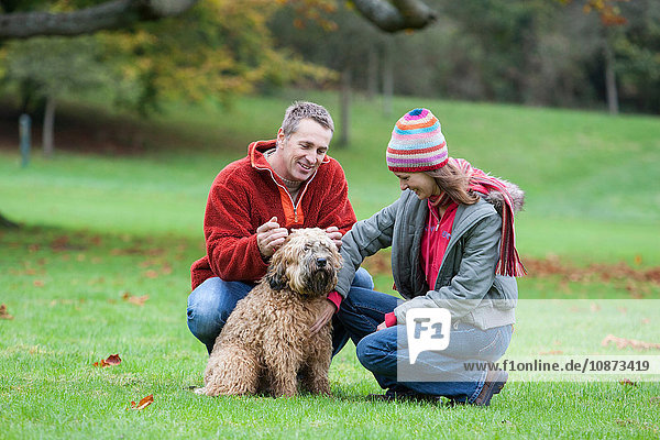 Heterosexual couple in park crouching stroking dog