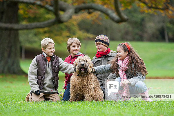 Vier Kinder im Park  kauernder  streichelnder Hund