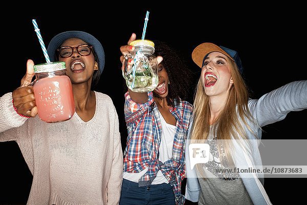Young women holding mason jars arms raised open mouthed smiling