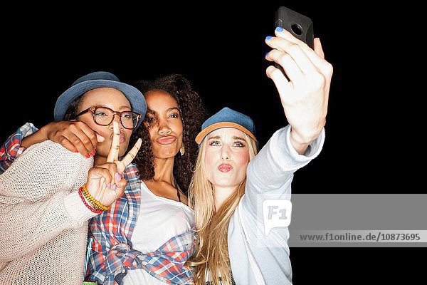 Young women huddled together making peace sign  puckering lips  using smartphone to take selfie
