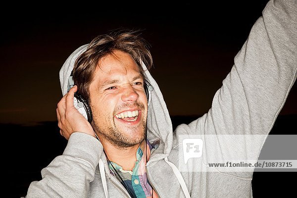 Young man wearing hoodie and headphones arm raised looking away smiling