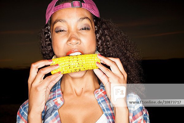 Junge Frau beißt Maiskolben auf den Kolben und schaut in die Kamera