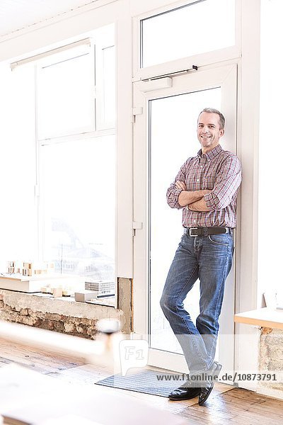 Full length view of mature man leaning against doorway arms folded looking at camera smiling