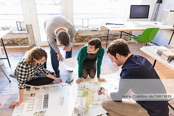 High angle view of architects on office floor discussing blueprint