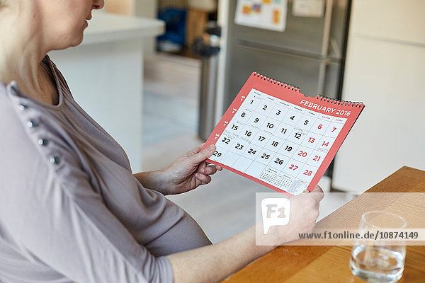 Hochwinkel-Seitenansicht einer schwangeren Frau beim Blick auf den Kalender