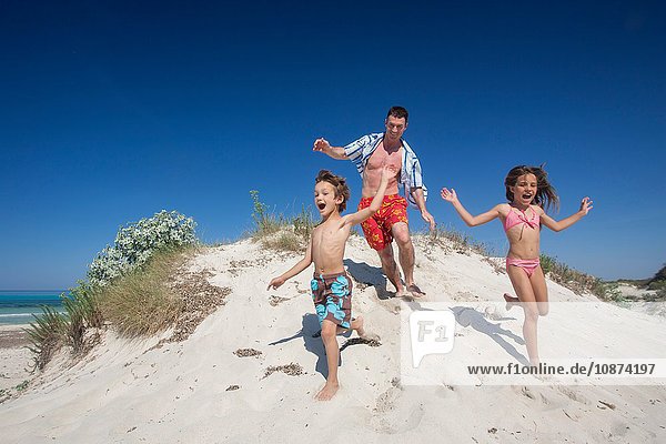 Mittelgroßer erwachsener Mann rennt auf Sanddüne mit Sohn und Tochter am Strand  Mallorca  Spanien