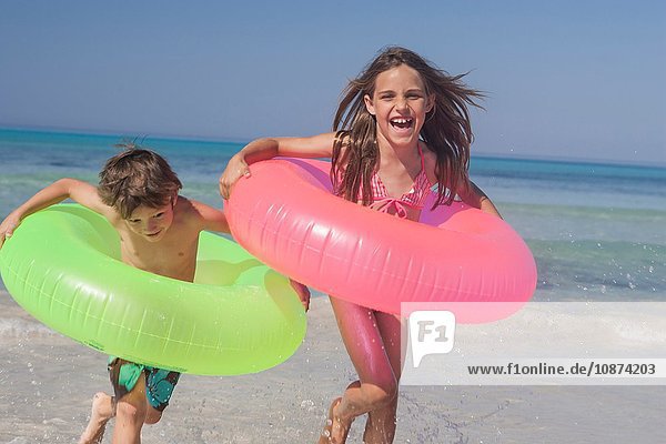 Mädchen und Bruder laufen am Strand mit aufblasbaren Ringen  Mallorca  Spanien