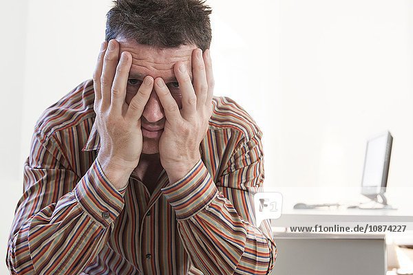Portrait of stressed businessman with hands over his face in office