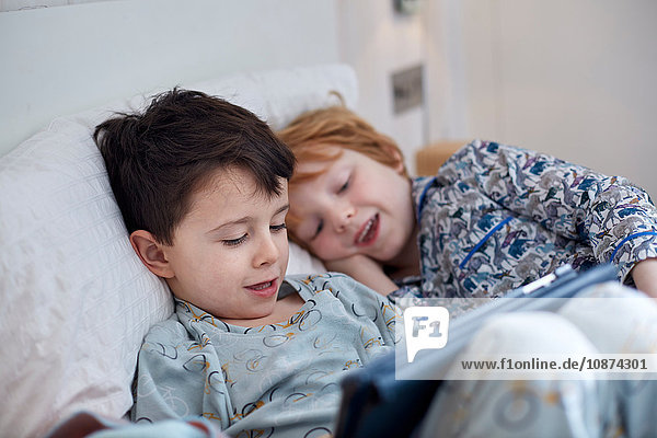 Jungen in Pyjamas mit digitalem Tablett im Bett