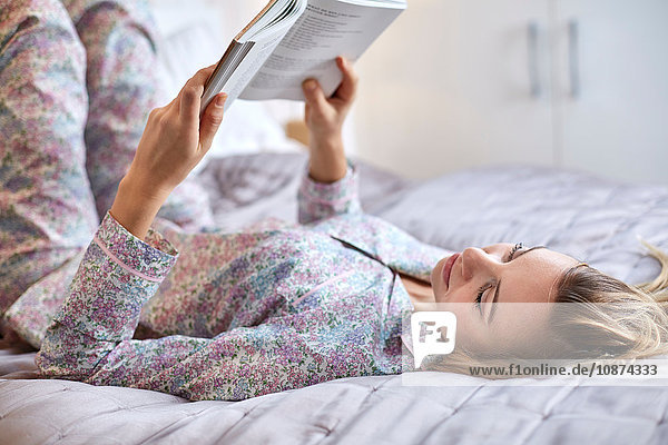 Frau im Schlafanzug liest Buch im Bett
