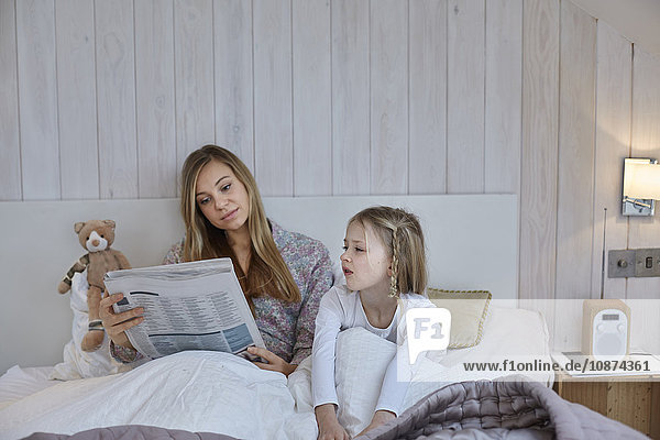 Mutter liest Zeitung neben Tochter im Bett