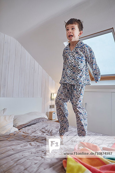 Junge im Pyjama springt im Hochzimmer auf das Bett