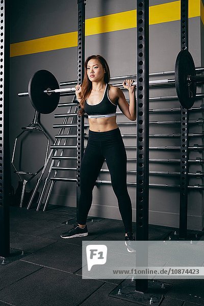 Junge Frau beim Gewichtheben mit Langhantel auf den Schultern im Fitnessstudio