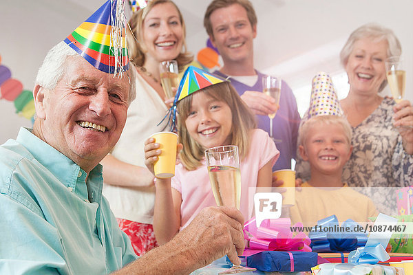 Mehrgenerationen-Familie schaut in die Kamera und bringt lächelnd einen Toast aus