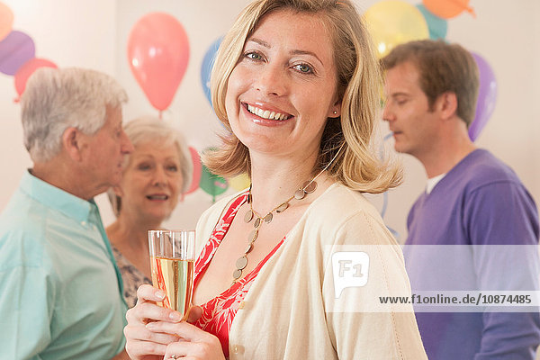 Frau auf der Party hält Champagnerflöte in der Hand und schaut lächelnd in die Kamera