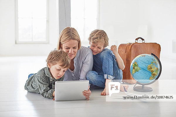Reife Frau und zwei Söhne sitzen auf dem Boden und schauen auf ein digitales Tablet