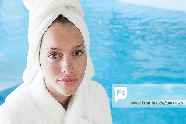 Portrait of beautiful young woman wearing white bathrobe by spa swimming pool