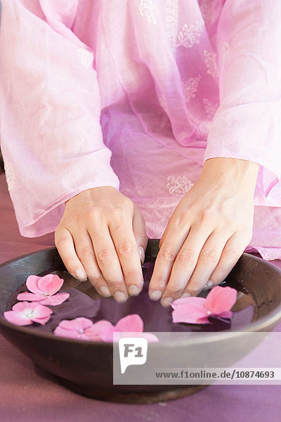 Cropped shot of young woman's fingernails soaking in bowl of flower petal water at spa