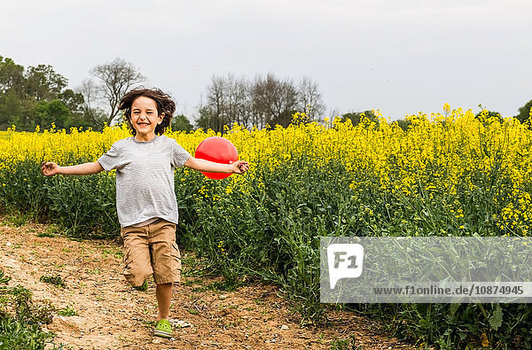 Junge rennt auf gelber Blumenfeldbahn und zieht roten Ballon