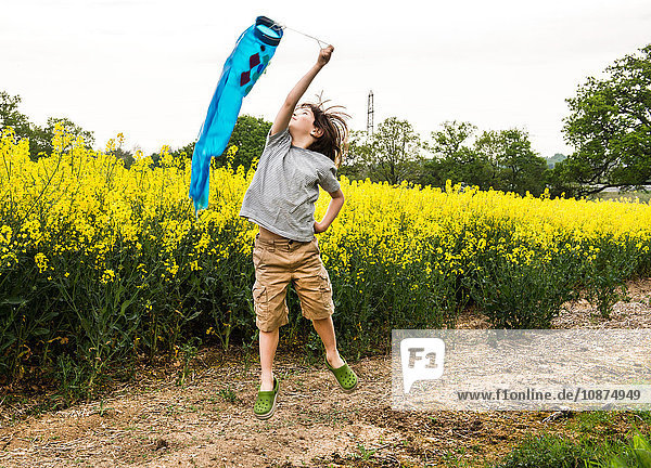 Junge springt auf gelber Blumenfeldbahn und zieht Fischdrachen