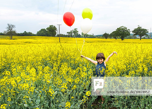 Junge steht in gelbem Blumenfeld und hält rote  gelbe und weiße Luftballons