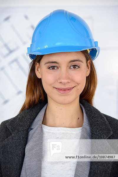 Porträt einer jungen Geschäftsfrau mit blauem Schutzhelm in neuem Büro