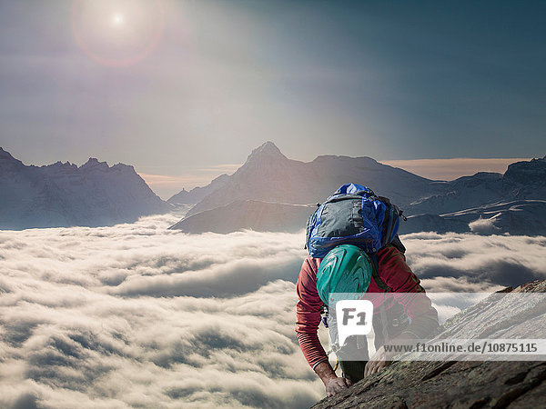Climber on a rocky wall above a sea of fog in an alpine valley  Alps  Canton Wallis  Switzerland