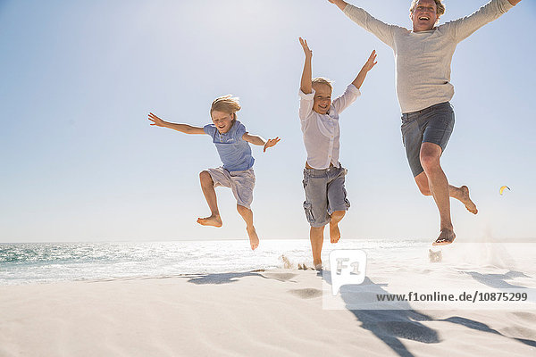 Father and sons on beach arms raised jumping in mid air